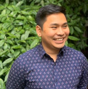 Azlan Nur Saidy standing in front of greenery. He is smiling into the distance and wearing a blue patternedshirt.