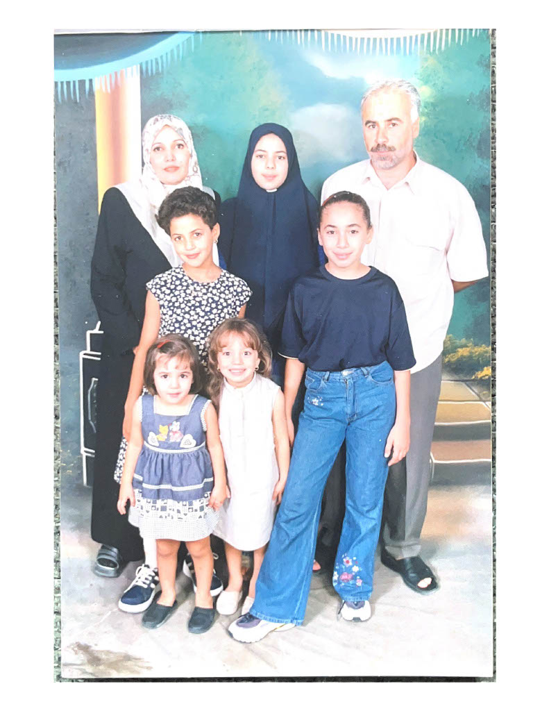 A family of six posing for the camera. Two of the people are wearing headscarves.